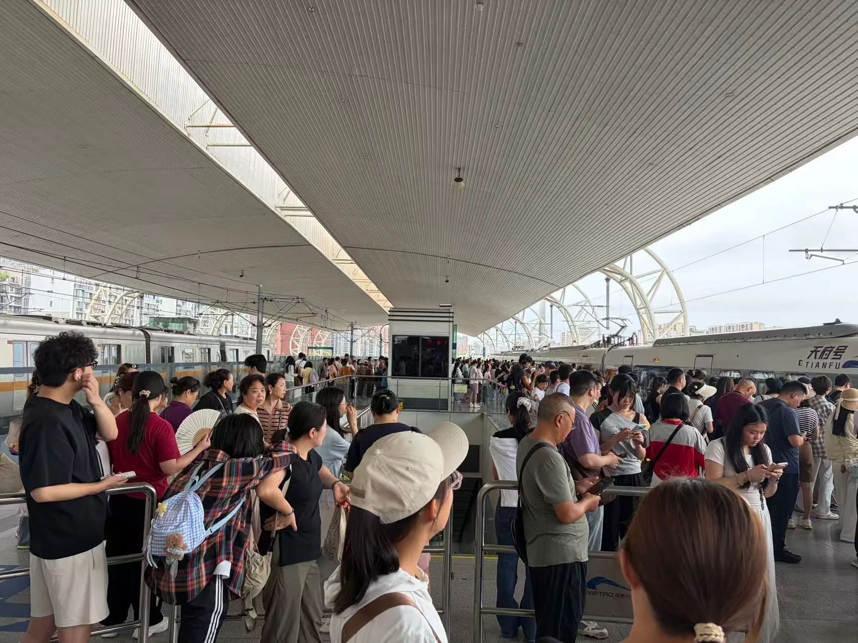 犀浦站站台上挤满了等车的人，旁边停着动车。