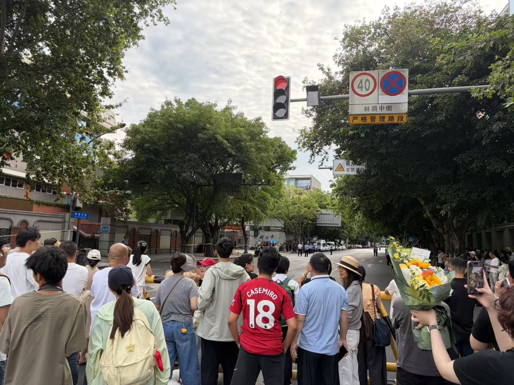 成都七中校门外等待的人群,树荫、红灯和一束花。